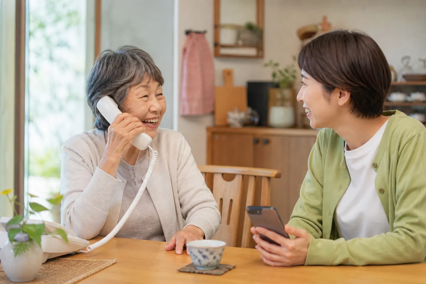 固定電話を使う高齢者とスマートフォンを持つ家族